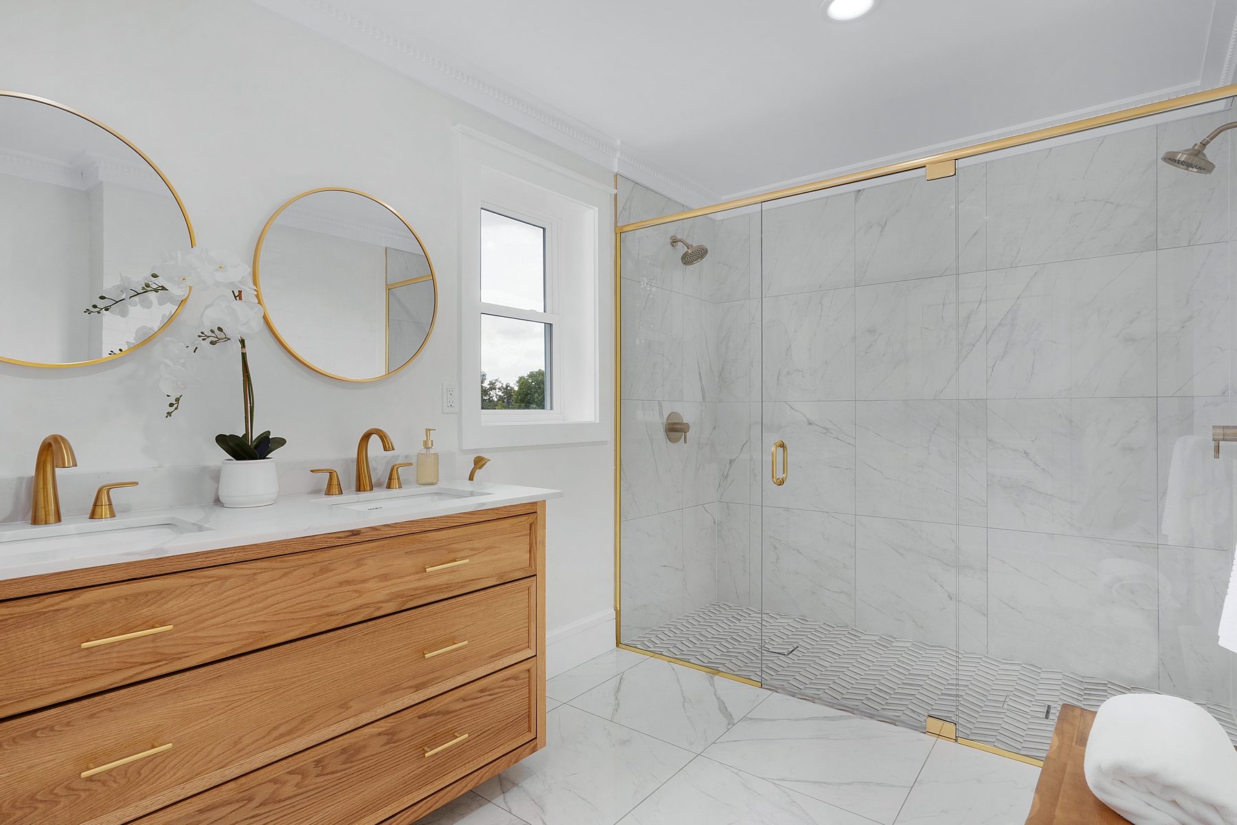 Bathroom with a floating white oak vanity, brass fixtures and a marble-tiled walk-in shower