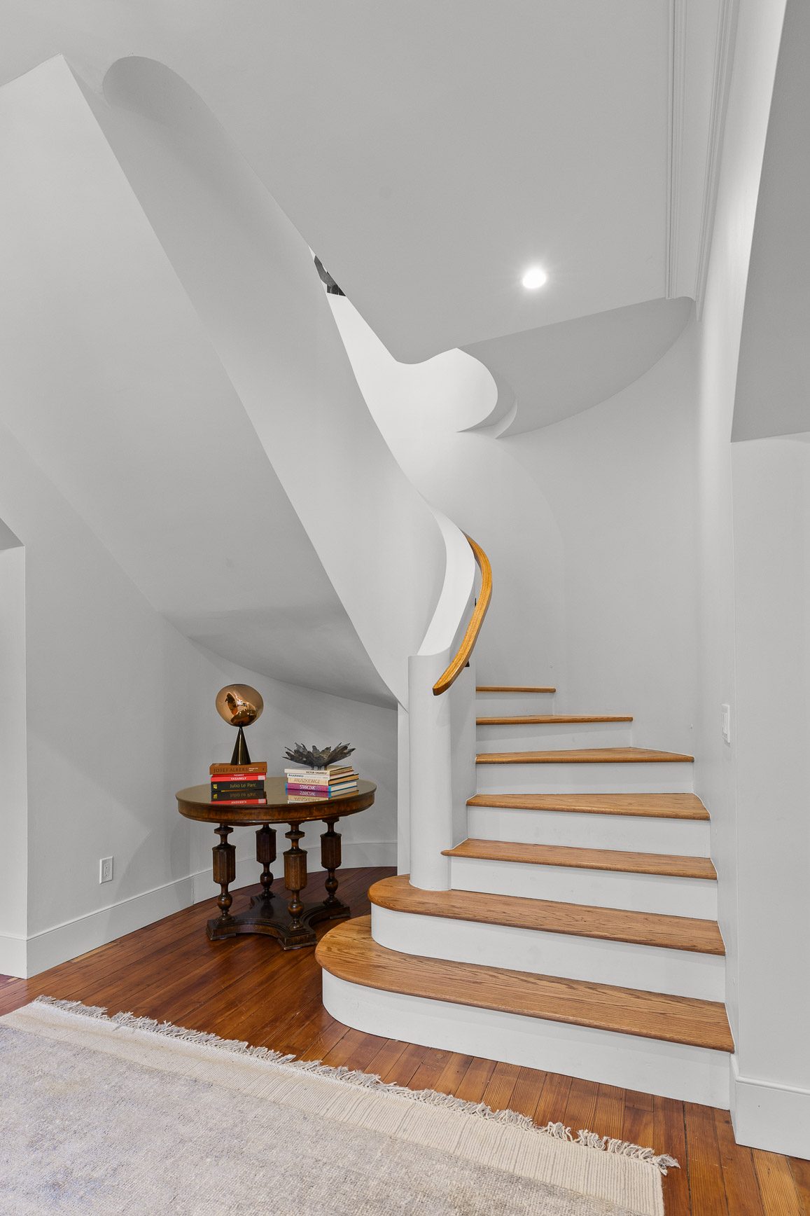 Curved white plaster staircase with white oak treads viewed from the entry