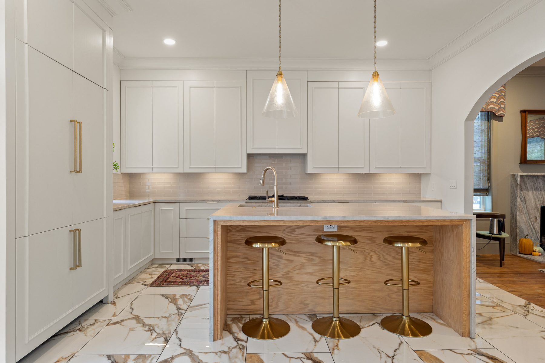 White oak kitchen island with fluted panelling and brass bar stools on Calacatta marble flooring