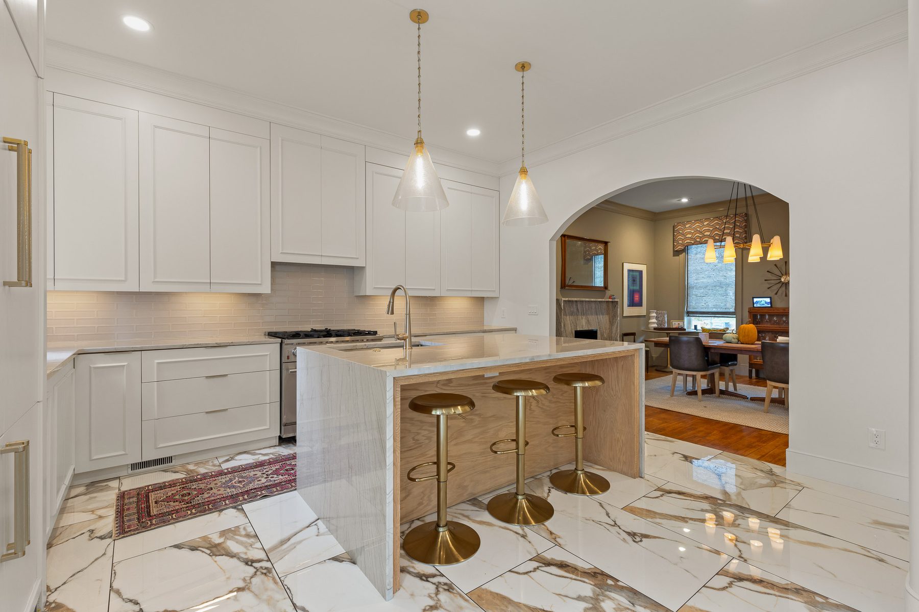 Remodelled kitchen opening through an arched doorway, in white cabinetry with marble flooring