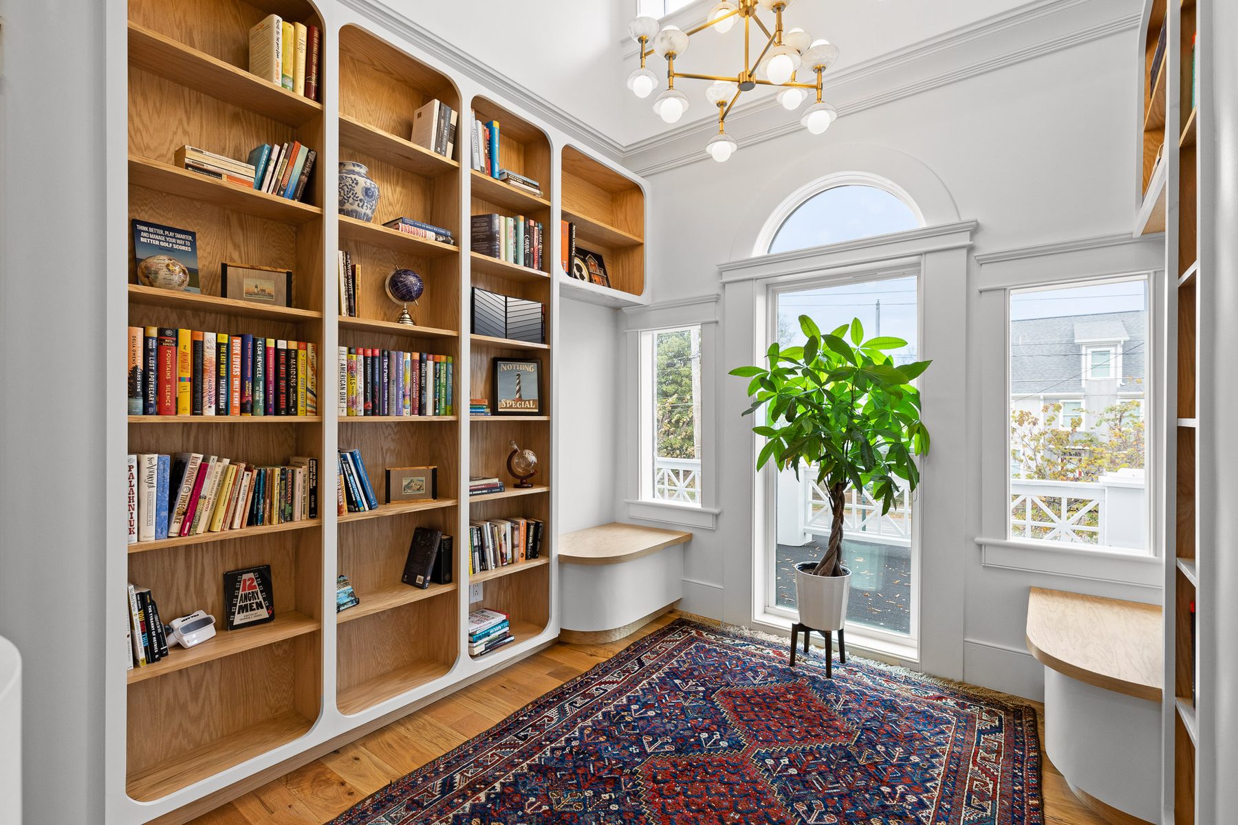 Floor-to-ceiling white oak library shelving with an arched window seat, lit by a brass chandelier, at 906 East Martin Luther King Boulevard