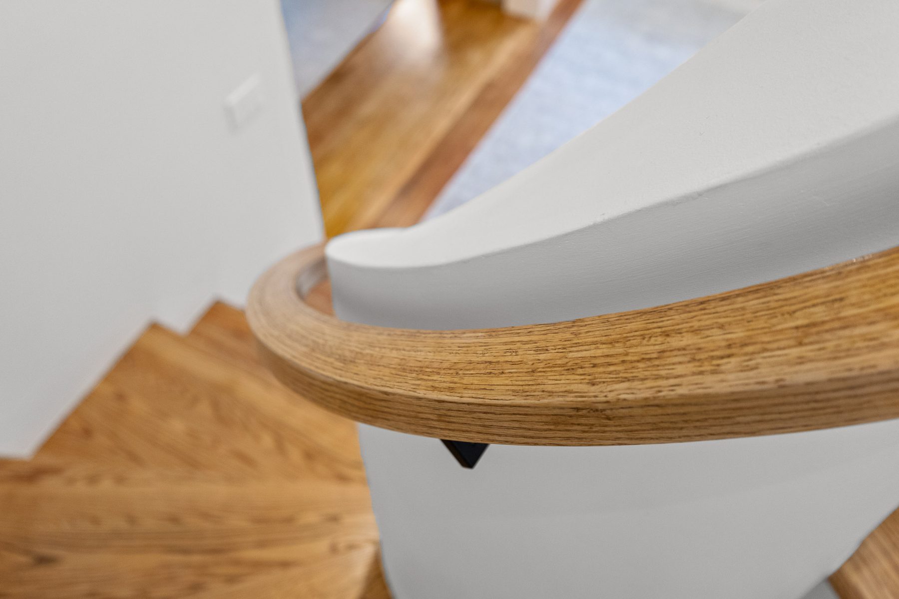 Hand-shaped oak handrail curving into the plaster wall of the restored staircase