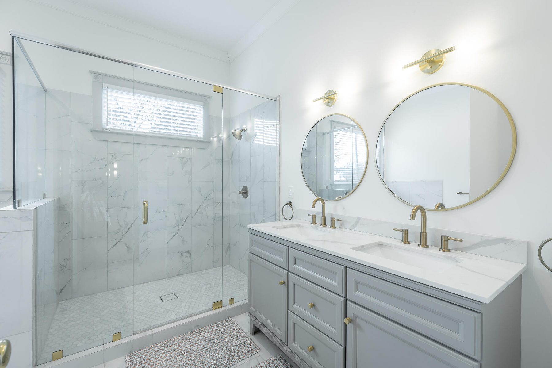 Renovated primary bathroom with a frameless marble shower and brass-framed mirrors