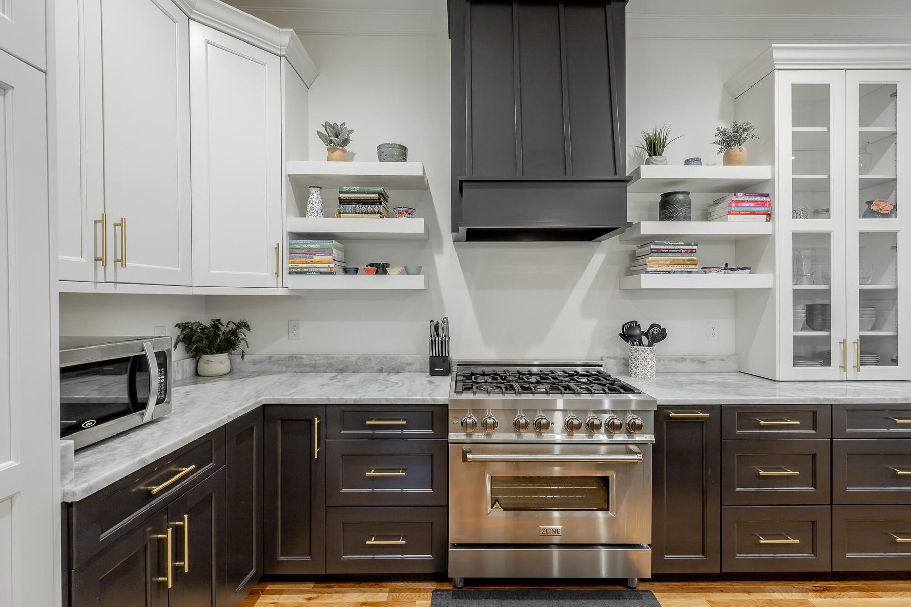Two-tone kitchen with a custom range hood and white marble counters on oak flooring
